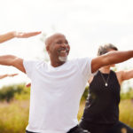 Group of older people stretching arms out for exercise. A smiling older man is centered in the photo