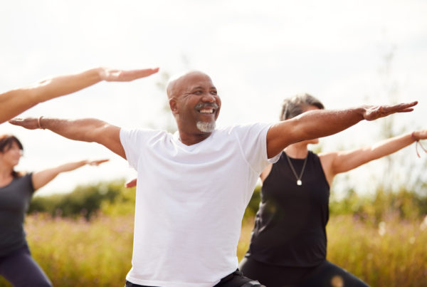 Group of older people stretching arms out for exercise. A smiling older man is centered in the photo