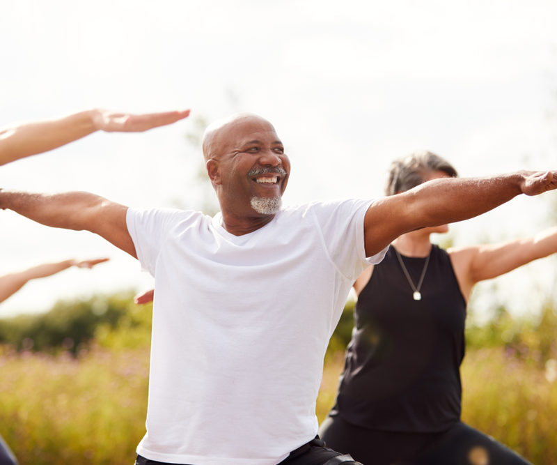 Group of older people stretching arms out for exercise. A smiling older man is centered in the photo
